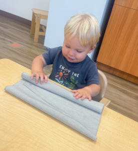 A Nido student focused on the task of rolling a work rug, developing a sense of order and motor coordination.
